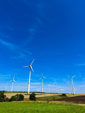Tall wind turbines spin in a green field under a blue sky, symbolizing our commitment to clean energy and sustainability for future generations in harmony with natureの写真素材