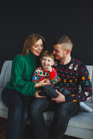A heartwarming family photo featuring a mom, dad, and their young son in festive sweaters, capturing the spirit of the holiday season in a cozy indoor atmosphere.の写真素材