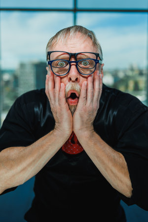 A man with glasses displays a surprised expression, capturing a moment of shock. Perfect for themes of surprise, emotions, and reactions in contemporary environments.の写真素材