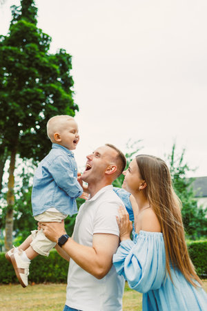 A joyful family enjoys a playful moment outdoors, with a father lifting his smiling child high while the mother shares in the laughter, embodying love and togethernessの写真素材