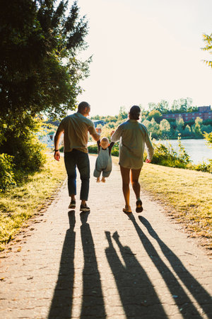 In a heartwarming scene, a joyful family is seen enjoying quality time together. The parents take turns swinging their delighted child on a beautiful sunny day beside the riverの写真素材