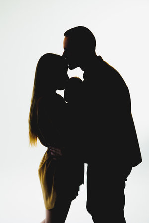 A stunning romantic silhouette of a couple sharing a tender kiss is beautifully highlighted against a soft, light background, perfectly embodying love, passion, and intimacyの写真素材