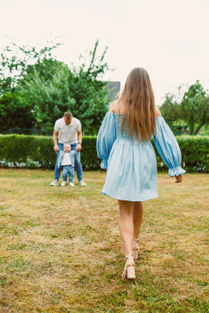 A heartwarming and joyful family scene unfolds as a loving mother walks towards her cheerful child and affectionate father in a serene garden, portraying love and togethernessの写真素材
