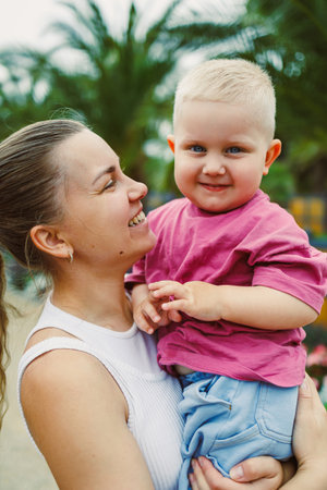 In a heartwarming and beautiful scene, a loving mother is joyfully holding her smiling and happy child, surrounded by vibrant greenery and a cheerful, delightful atmosphereの写真素材