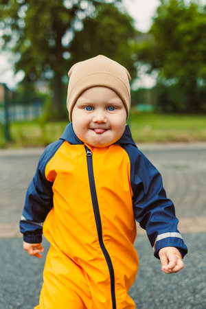 A cheerful toddler in a bright orange rain suit and tan hat plays outside, embodying the spirit of...