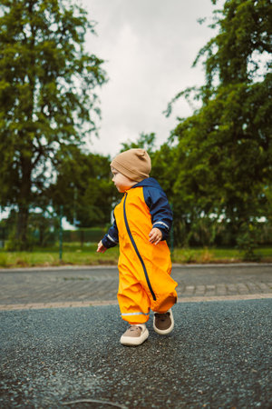A cheerful, happy child dressed in a bright yellow rain suit joyfully walks along a slippery path, embodying the carefree essence of childhood and the thrill of exploring natureの写真素材