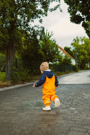 A cheerful child, clad in bright and vibrant rain gear, joyfully enjoys running down an empty...