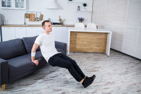 A man skillfully executes tricep dips on a sleek sofa in a chic, modern living room, showcasing...