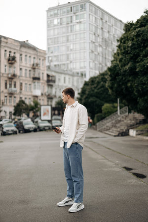 A stylish young man checks his smartphone on a bustling city street, framed by striking architecture...