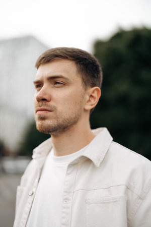 A stylish young man confidently poses in an urban environment, showcasing his modern aesthetic while displaying a thoughtful expression and wearing contemporary fashionの写真素材