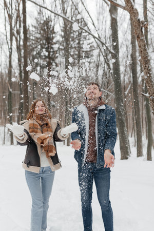 A cheerful couple frolics in a snowy forest, creating a joyful winter scene filled with love and...