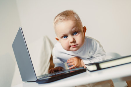 A cute baby with bright blue eyes curiously exploring a laptop on a modern desk. The minimalist...