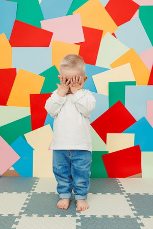 A cute young child covers their eyes in a playful game of peekaboo, surrounded by vibrant...