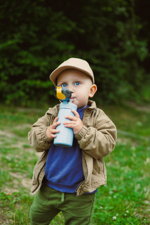A cheerful toddler in warm clothing plays outside with a colorful water bottle, surrounded by lush...
