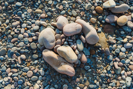 Smooth pebbles of various shapes and sizes cover the beach, glistening under the sun, creating a...