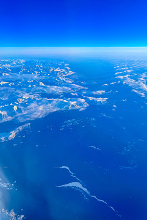 Breathtaking landscape showcases towering, snow-capped mountains rising from clear blue ocean under a vibrant sky, creating a serene atmosphere from high above.の写真素材