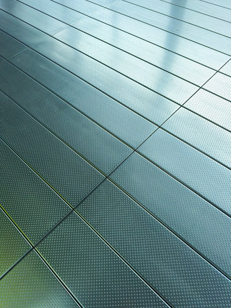 A contemporary floor with a shiny metallic surface reflects sunlight and shadows, showing a mix of textures and creating an artistic visual effect in a bright setting.の写真素材