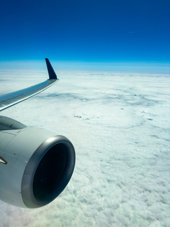 A jet wing and engine frame the view of endless white clouds under a brilliant blue sky, signifying...