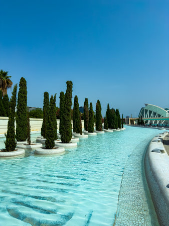 Tall trees line the edge of a sparkling blue body of water, creating a serene atmosphere. Modern...