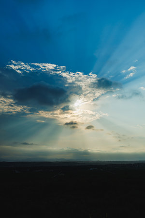 Golden rays of sunlight pierce through soft clouds, illuminating a tranquil horizon while casting...