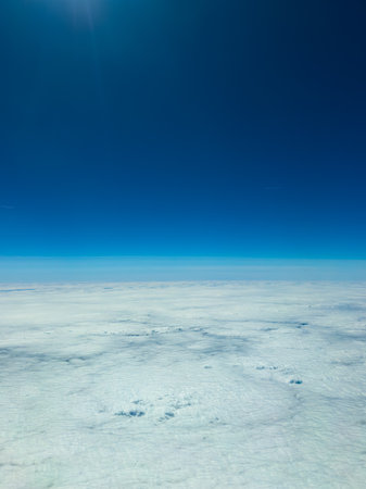 Fluffy white clouds blanket the earth below, while a vibrant blue sky frames the scene high above,...