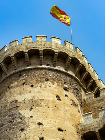 The robust stone tower stands tall against the vibrant blue sky, topped with a waving flag. Details of weathered stone reflect the history and strength of the structure.の写真素材