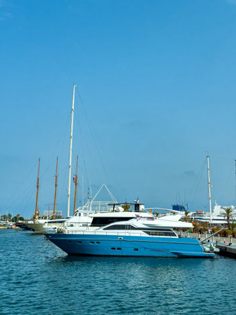 A luxury yacht sits peacefully at the marina, surrounded by smaller boats under a clear blue sky. The calm water reflects the sunny daytime atmosphere.の写真素材