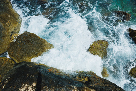 Powerful waves break against the jagged rocks near the coast, creating a beautiful display of foam...