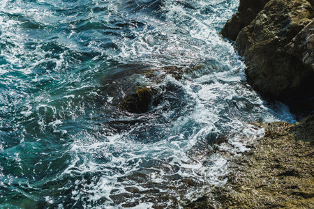Waves gently collide with rugged rocks along the coastline, creating a calming scene of nature's...