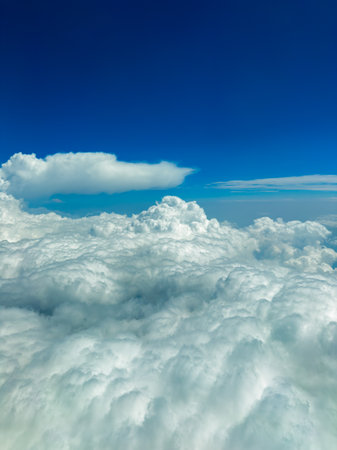 Fluffy white clouds form a soft blanket under a bright blue sky, creating a serene scene during a peaceful afternoon flight high above the earth.の写真素材