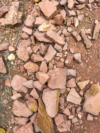 Dry ground showcases an array of red and brown stones scattered across the surface, creating a natural mosaic. Sunlight highlights the rugged textures of the rocks.の写真素材