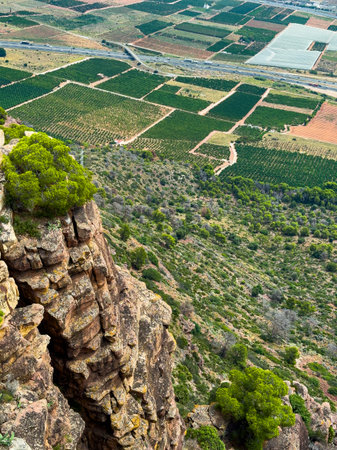 From a high cliff, lush green vineyards stretch across the valley below, surrounded by rolling hills...