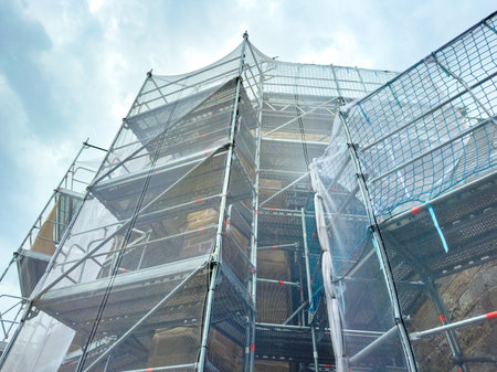 Metal scaffolding surrounds a building under renovation, towering high into the overcast sky, while workers carry on with their tasks, creating a sense of progress and transformation.の写真素材