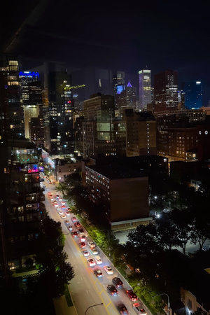 Cars stream through the bustling streets below, their headlights illuminating the night. Tall buildings tower above, reflecting the city's electric vibe and colorful lights.の写真素材