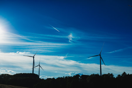 Wind turbines stand tall against a backdrop of vibrant blue sky and soft clouds during sunset,...