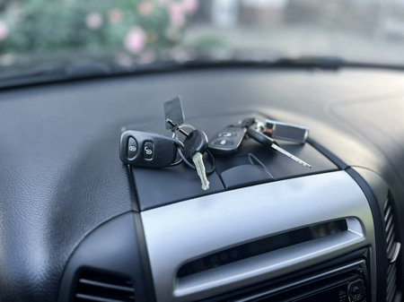 Keys lie on the dashboard of a parked car, catching the soft morning light. Nearby, vibrant flowers bloom, adding color to the serene outdoor scene.の写真素材