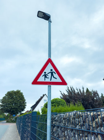 Bright warning sign indicates a children's crossing area beside a quiet neighborhood street under an overcast sky, promoting safety for young pedestrians.の写真素材