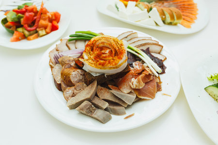 A vibrant display of assorted meats and vegetables garnished with green onions, served on a round white platter during a joyful celebration with family and friends.の写真素材