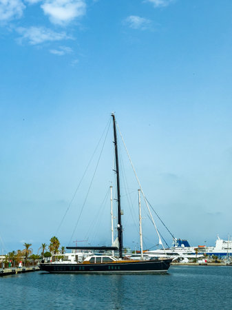 A sailing yacht is anchored in a marina surrounded by other boats. The clear blue sky reflects the tranquility of the afternoon, inviting relaxation by the water.の写真素材