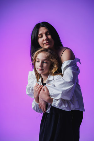 In a soothing purple glow, a mother holds gently her daughter, creating a heartfelt scene of intimacy. Their love radiates in this perfect moment of togetherness and joy.の写真素材