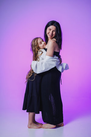 A mother hugs her daughter tightly in a playful pose, both smiling. The purple background adds a playful vibe, capturing a moment of love and happiness between them.の写真素材