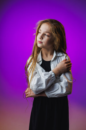 A young girl with long hair stands with her arms crossed, wearing a loose white shirt and a black dress.の写真素材