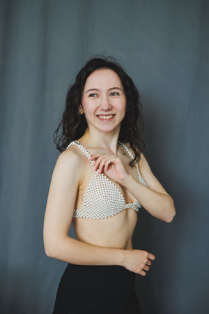 A cheerful woman stands confidently, showcasing a creative design. With curly hair and a bright smile, she exudes a playful spirit amidst a simple gray backdrop.の写真素材