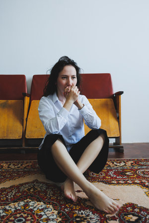 A young woman with dark hair sits cross-legged on a vibrant rug, her bare feet touching the soft...