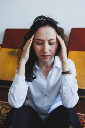 A thoughtful woman with curly hair rubs her temples in a quiet room, reflecting on her thoughts. The...