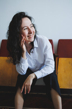 Curly-haired woman sits comfortably on wooden bench, resting her chin on her hand while smiling. The bright atmosphere highlights her joyful demeanor in the relaxed setting.の写真素材