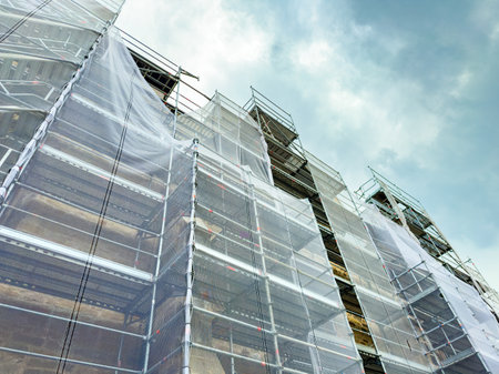 Workers are busy on a construction site, surrounded by towering scaffolding and white protective...