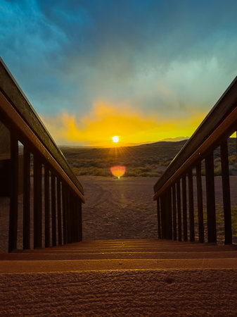 Golden sunset illuminates the horizon as seen from a set of wooden stairs in a peaceful desert setting, with colors blending beautifully in the sky.の写真素材