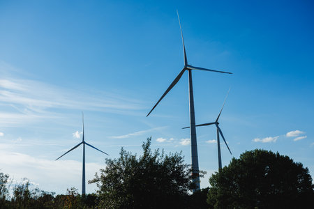 Three large wind turbines rotate gently in the wind, surrounded by lush greenery and under a clear...