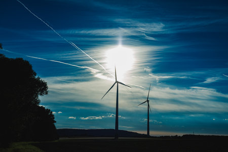 Wind turbines illuminate under a vibrant sky as the sun sets, casting striking shadows and highlighting the beauty of renewable energy in a serene landscape.の写真素材